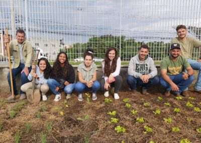 Sete alunos do curso de Engenharia Agronômica da Facens, em frente a uma horta com mudas plantadas